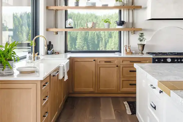 Modern kitchen interior featuring wooden cabinets, a white countertop, and open shelving with plants, emphasizing a clean and functional design for effective home maintenance.