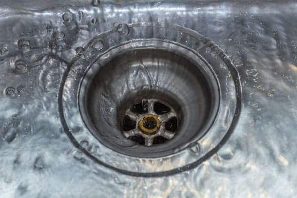 Drain in a kitchen sink with water swirling around, illustrating the importance of drain maintenance and cleaning for homeowners.