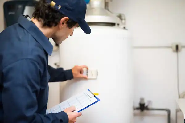 HVAC technician inspecting a water heater and checking maintenance notes for plumbing services.