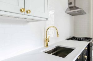 Modern kitchen featuring a stainless steel sink with a sleek gold faucet, white cabinetry, and a gas stove, illustrating a stylish environment for garbage disposal installation and replacement.