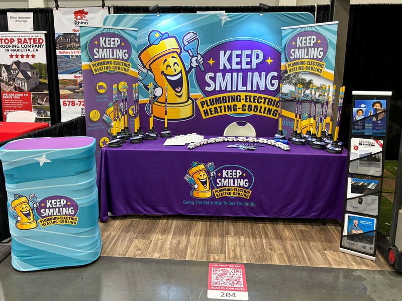 Keep Smiling Plumbing Electric Heating and Cooling booth at a Home Show, featuring colorful branding, promotional materials, and engaging displays for plumbing, electrical, and HVAC services.